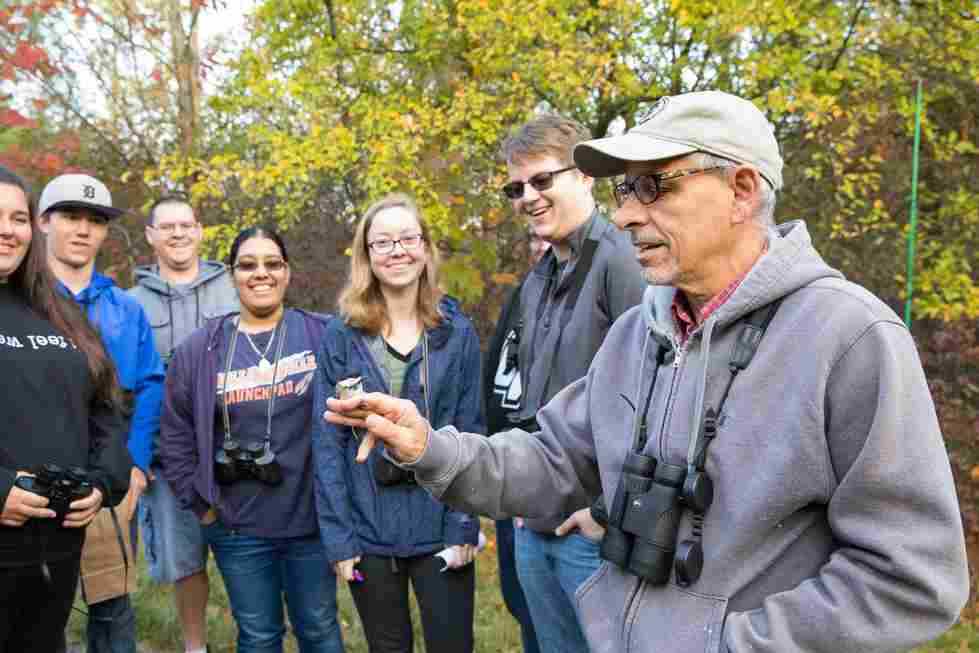 Professor showing a group of students a bird sitting on his finger while outside on Grand Valley's campus.